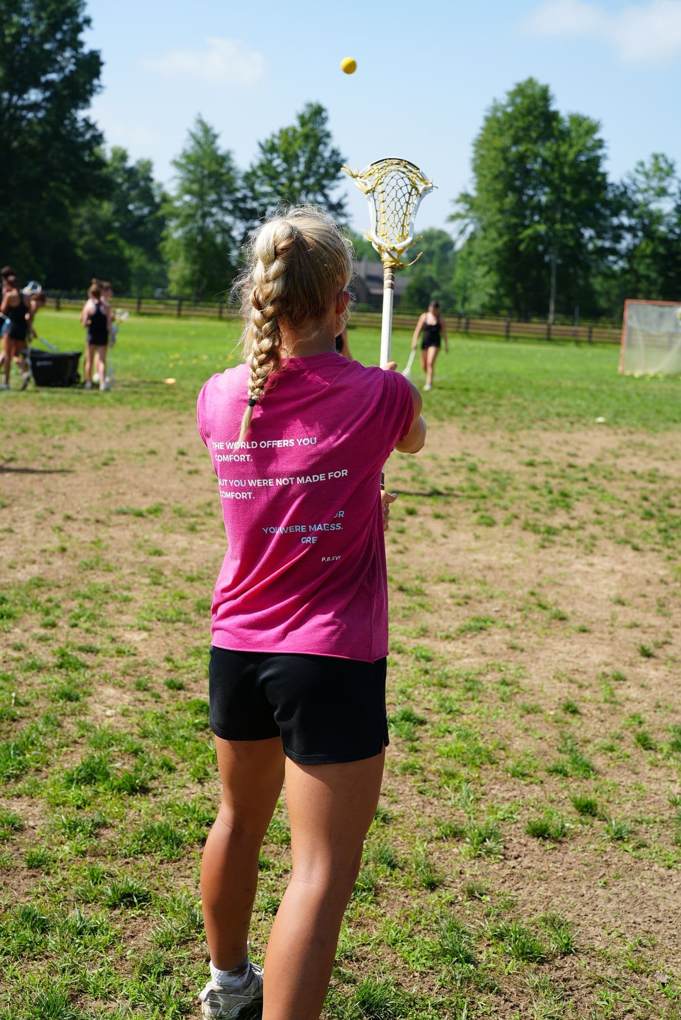 An athlete in a pink shirt throws a ball against the wall with her stick.